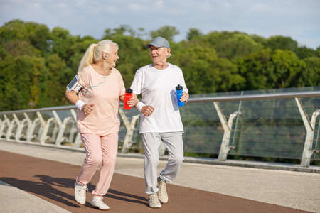 Happy senior couple with bottles runs training together on footbridgeの写真素材