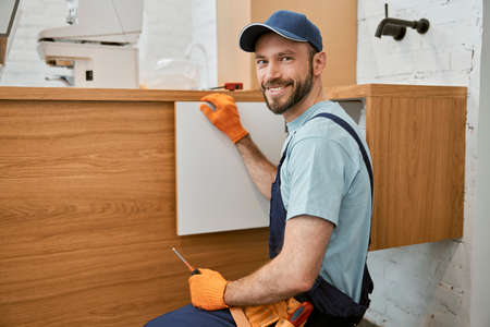 Cheerful male worker fixing cupboard door in kitchenの写真素材