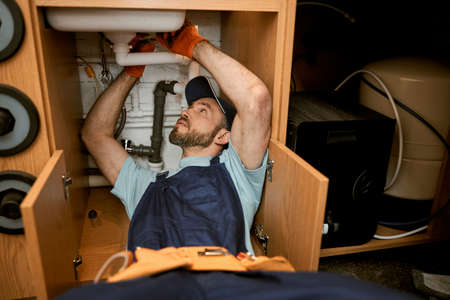 Male plumber repairing sink pipe in kitchenの写真素材