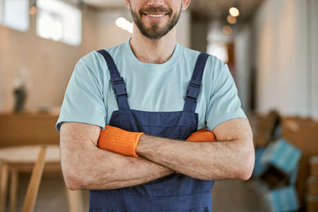 Cheerful male worker in gloves keeping arms crossedの写真素材