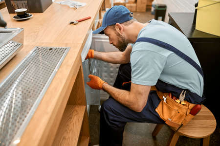 Bearded young man repairing fridge in cafeの写真素材