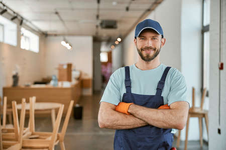 Joyful male worker in cap keeping arms crossedの写真素材