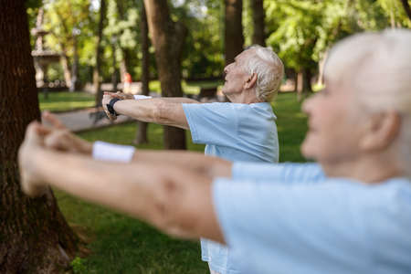 Grey haired mature man trains with woman on meadow in city parkの写真素材