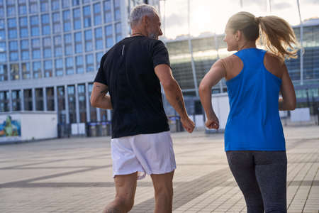 Back view of middle aged couple in sportswear full of energy jogging together in urban environment in the morningの写真素材
