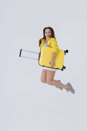 Cheerful young woman with travel bag jumping in studioの写真素材
