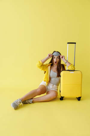 Shocked woman in sleep mask sitting near travel bagの写真素材
