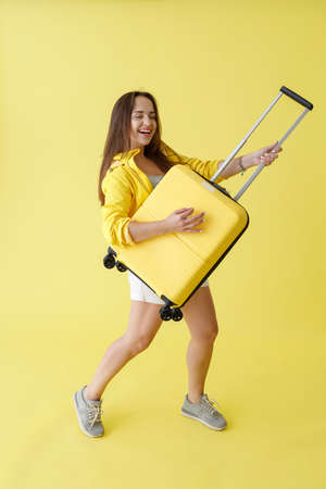 Joyful woman with trolley luggage bag standing in studioの写真素材