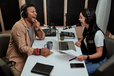 Portait of two cheerful radio hosts, young man and woman laughing while discussing various topics, reading a script, moderating a live show in studioの写真素材