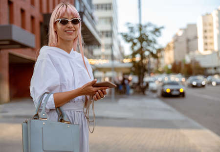 Joyful woman standing on the street and holding cellphoneの写真素材