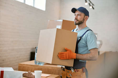 Bearded young man in gloves holding cardboard boxの写真素材