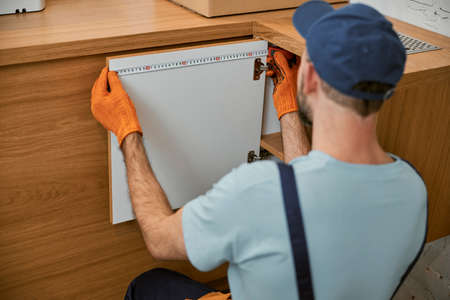 Male worker measuring cupboard door in kitchenの写真素材