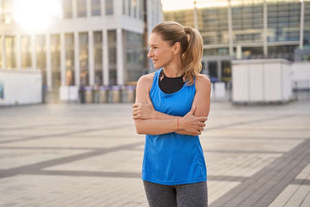 Beautiful middle aged woman in sportswear looking aside while standing outdoors, ready for workout in the cityの写真素材