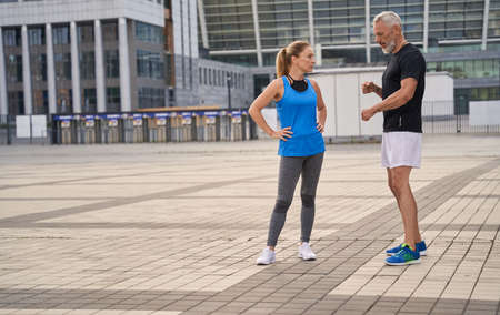 Full length shot of two sportive friends, middle aged man and woman in sportswear talking while standing outdoors, having morning workoutの写真素材