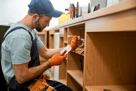 Bearded young man repairing desk electrical wiresの写真素材