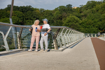 Senior woman and man with mats and bottles rest standing on footbridgeの写真素材