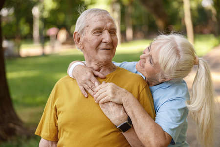Sportive senior woman hugs friend training together in green parkの写真素材
