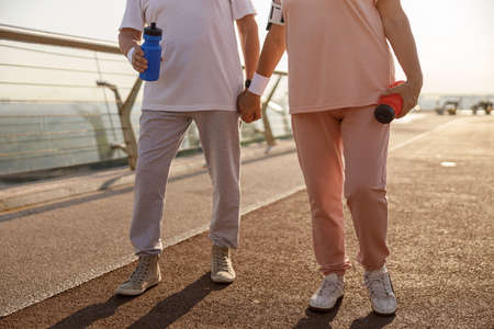 Mature couple in sportswear with bottles stands on city footbridge in eveningの写真素材