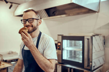 Bearded man in apron smelling pastry in cafeの写真素材