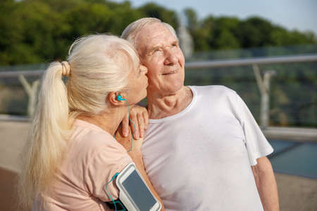 Senior woman with ponytail kisses happy husband at training on footbridge