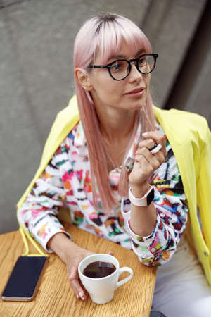 Female with dyed hair sitting at cafe with coffee cupの写真素材