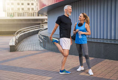 Full length shot of happy middle aged couple, man and woman in sportswear smiling, standing together outdoors ready for workoutの写真素材