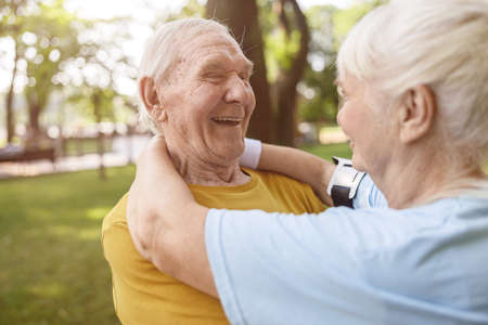 Laughing senior man embraces beloved wife standing in green park
