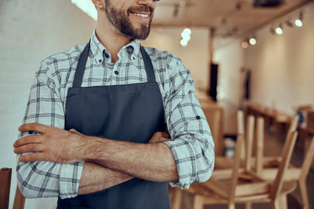 Joyful bearded man in apron keeping arms crossedの写真素材