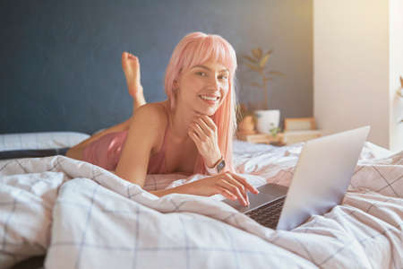 Beautiful lady spends time using modern laptop on large bedの写真素材