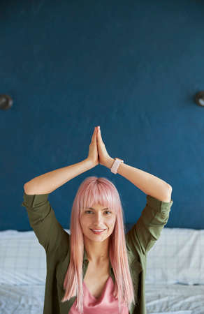 Long haired woman holds hands in namaste mudra above head in bedroomの写真素材