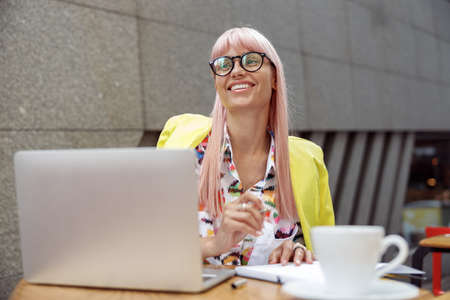 Happy woman in yellow blazer sitting in cafe with notebookの写真素材
