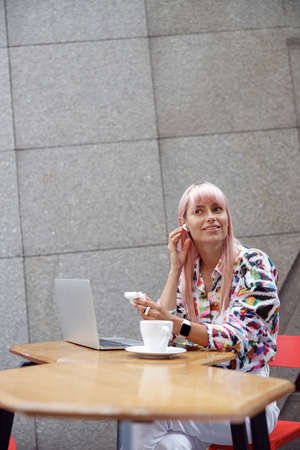 Woman putting earbud into her right ear in cafeの写真素材