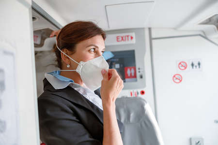 Female flight attendant putting on medical mask in aircraftの写真素材