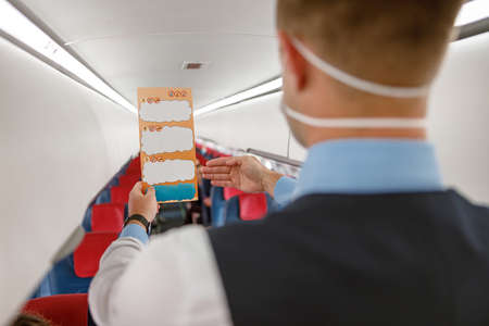 Male flight attendant with paper booklet standing in airplane salonの写真素材