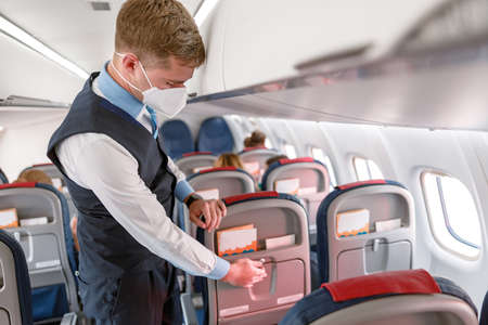 Flight attendant in face mask preparing passenger seat in airplaneの写真素材