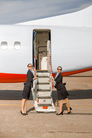 Smiling stewardess standing near airplane and inviting on boardの写真素材
