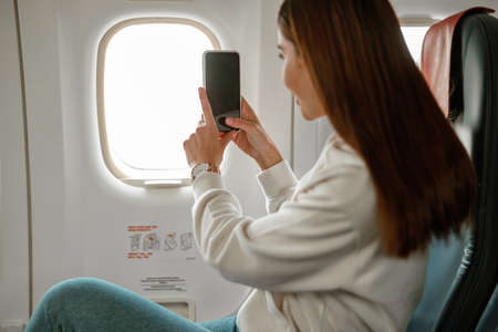 Young woman taking photo with smartphone in airplane