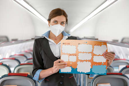 Female flight attendant in face mask holding instruction bookletの写真素材