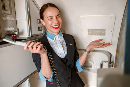 Cheerful flight attendant with telephone standing in aircraft cabinの写真素材