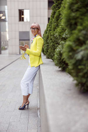 Cheerful woman with cellphone standing on the streetの写真素材
