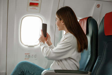 Female traveler taking picture with mobile phone in aircraftの写真素材