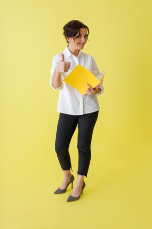 Cheerful woman holding documents and giving thumbs upの写真素材