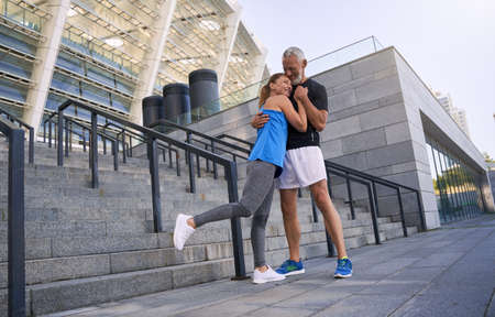 Full length shot of lovely sportive middle aged couple, man and woman in sportswear embracing while standing together outdoors. Sport, healthy lifestyle conceptの写真素材