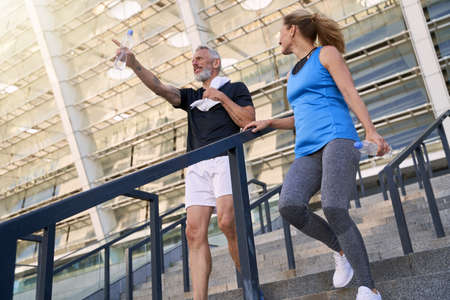 Low angle view of mature couple, man and woman in sportswear walking down the stairs after working out together outdoorsの写真素材