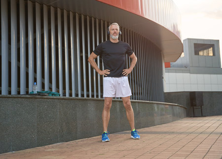 Full length shot of active middle aged sportsman in sportswear and headphones warming up, getting ready for workout outdoorsの写真素材