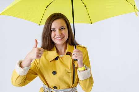 Joyful young woman holding umbrella and giving thumbs up