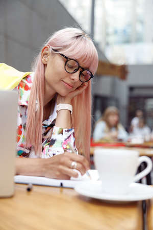 Focused female making notes in her notepad in street cafeの写真素材