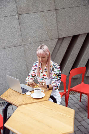 Stylish woman clicking her mobile phone at cafe table outsideの写真素材