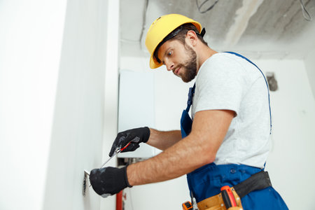 Male worker professional electrician in uniform installing electrical outlet in apartment after renovation workの写真素材