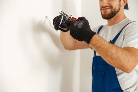 Hands of electrician using pliers while cutting wires, working on residential electric system in new houseの写真素材