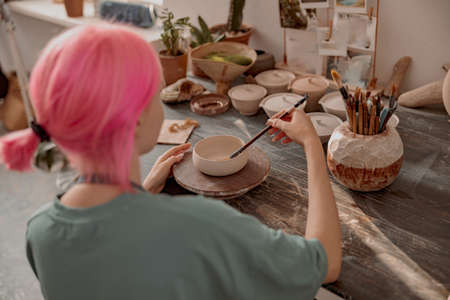 Female ceramist decorating earthenware in ceramic workshopの写真素材